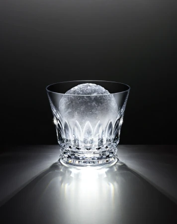 Crystal glass with faceted design, filled with crushed ice, against a dark backdrop and illuminated from below, casting shadows.