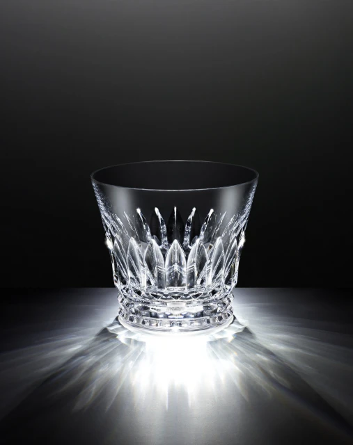 Elegant crystal ice bucket with intricate cut glass design, illuminated by bright lighting against a gradient black background.
