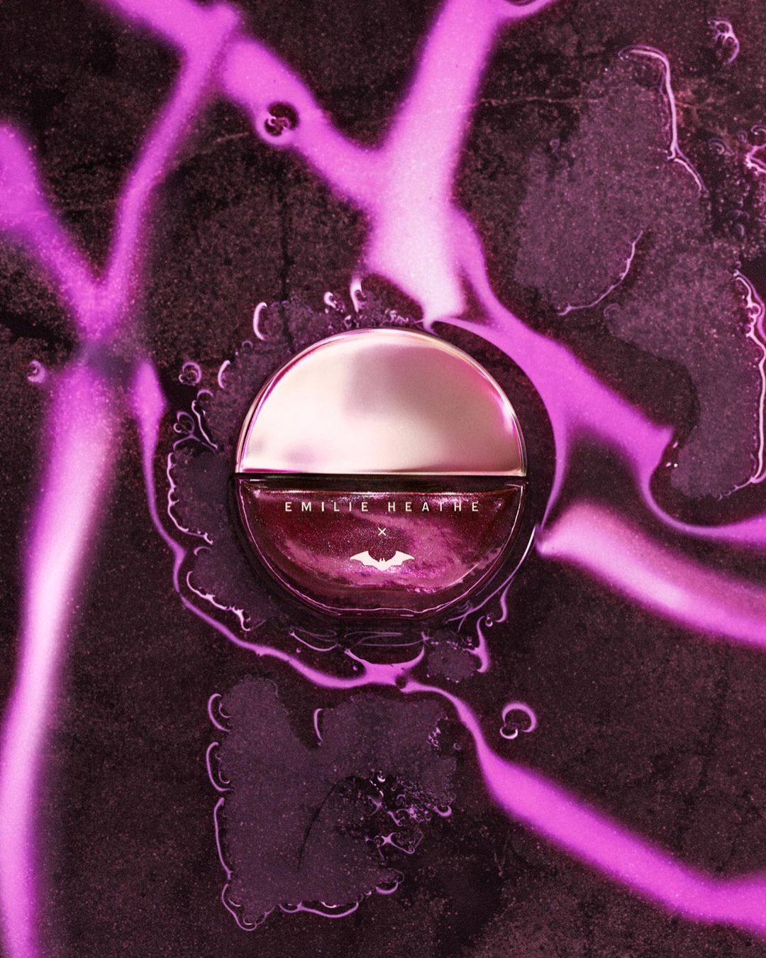 Close-up studio shot of a bottle of Emilie Heathe nail polish surrounded by water droplets on a black marble surface with pink lighting.