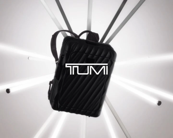 Black quilted backpack with the white TUMI logo in the center floating against a white background and lit by white light beams.