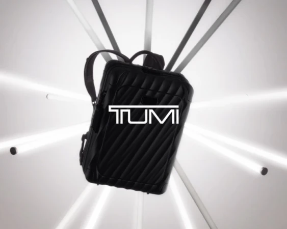 Black quilted backpack with the white TUMI logo in the center floating against a white background and lit by white light beams.
