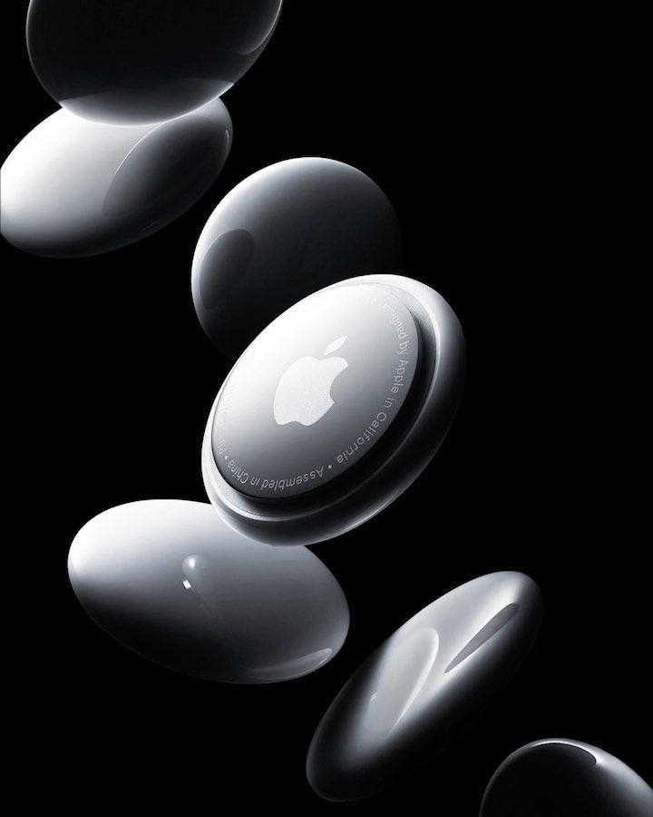 Multiple white Apple AirTags are suspended mid-air against a dark background, emphasizing their minimalist design and technology.