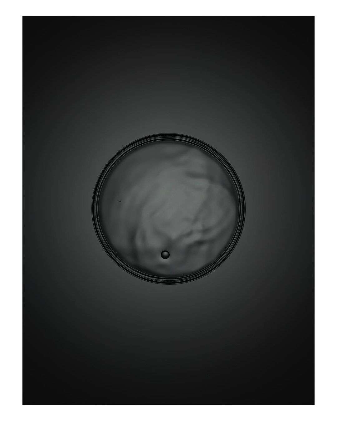 Close-up of a petri dish with fluid and a small bubble in the center, set against a dark gray background with bright spot lighting.