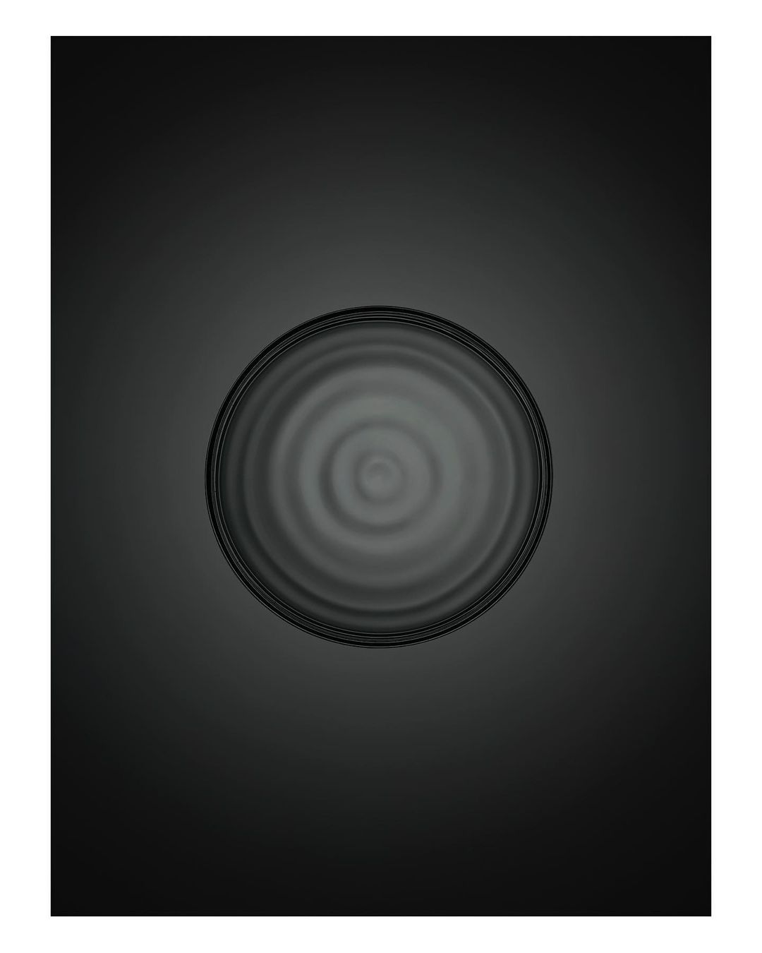 Overhead shot of a circular glass bowl on a dark grey surface with radial liquid patterns, creating a simple, minimalist composition.