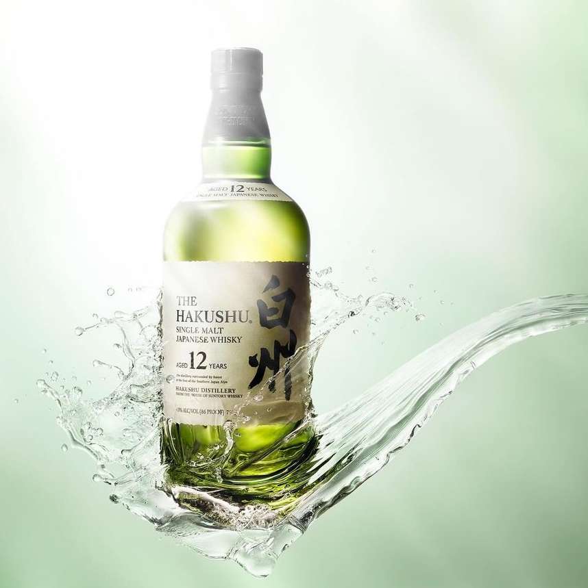 Bottle of Hakushu Japanese whisky with water splash effect on a light green background, product shot for advertising and marketing.