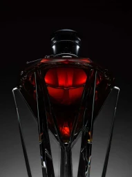 Close-up product shot of a dark red faceted crystal luxury perfume bottle lit dramatically on a dark background.
