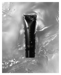 Black hand cream tube submerged in swirling water with bubbles, photographed vertically in monochrome.