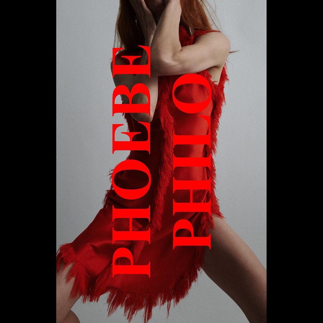 Woman in a fringed red dress poses in front of a grey wall with vertical red text overlaying the subject.