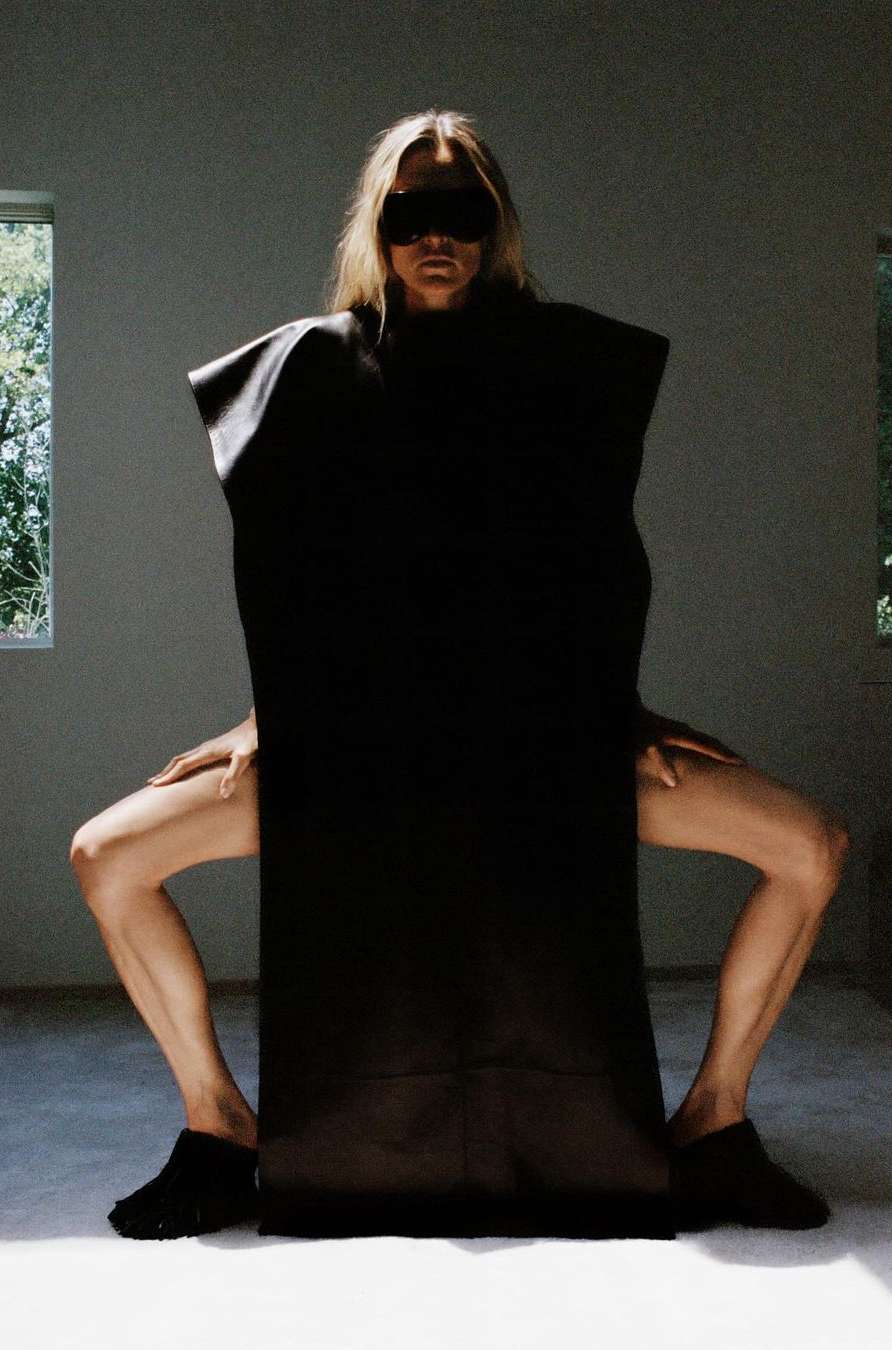 Person draped in black cloth, posed in an interior space with window light, creating a stark and visually striking composition.