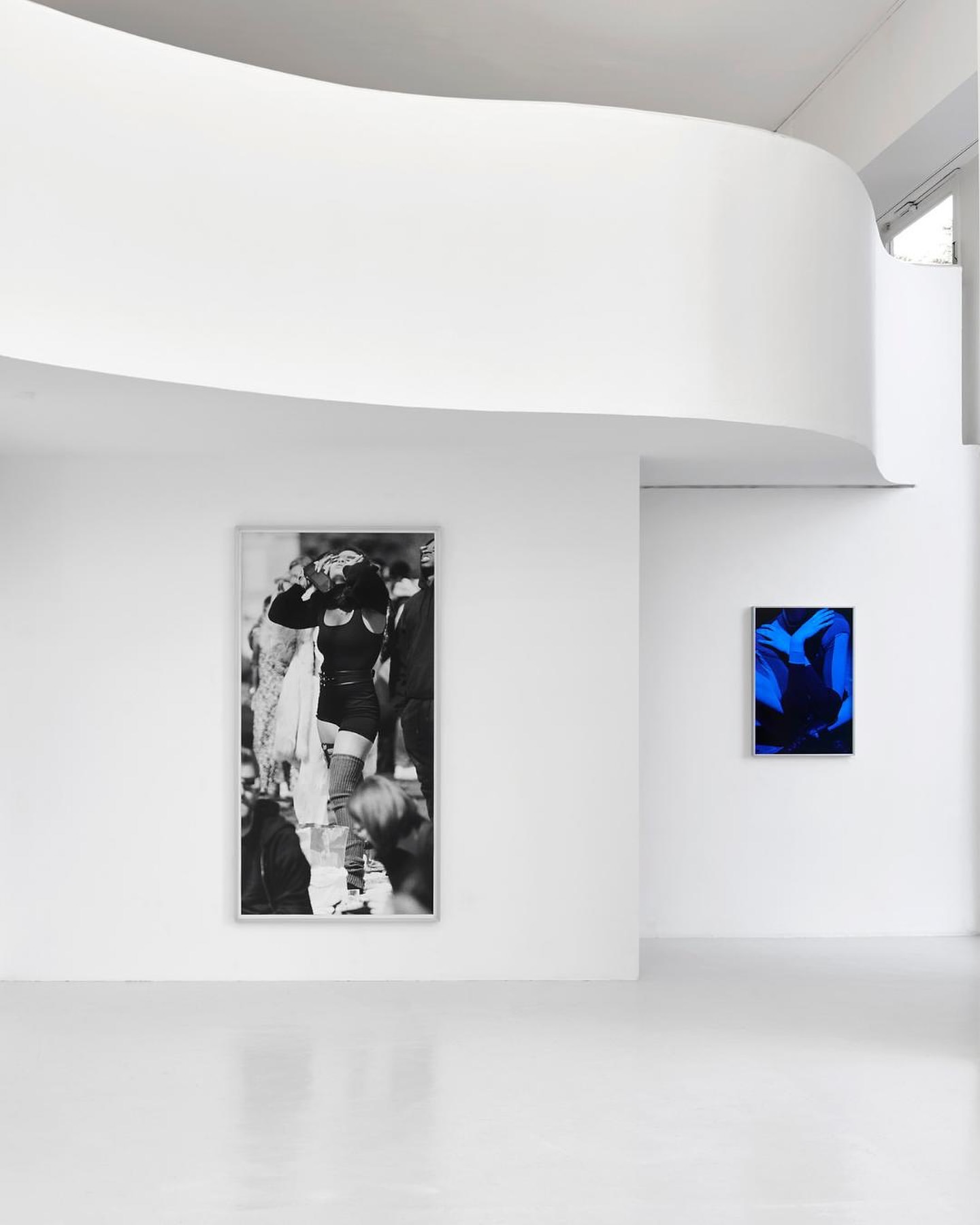 Art gallery interior featuring a black and white fashion photograph and a vibrant blue abstract artwork displayed on white walls.