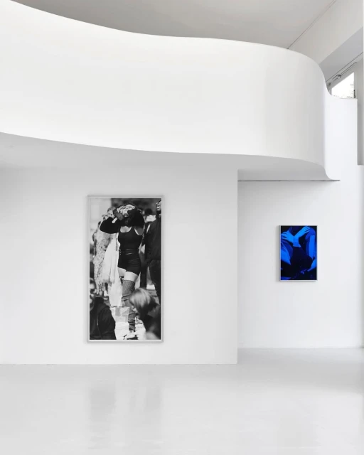 Art gallery interior featuring a black and white fashion photograph and a vibrant blue abstract artwork displayed on white walls.