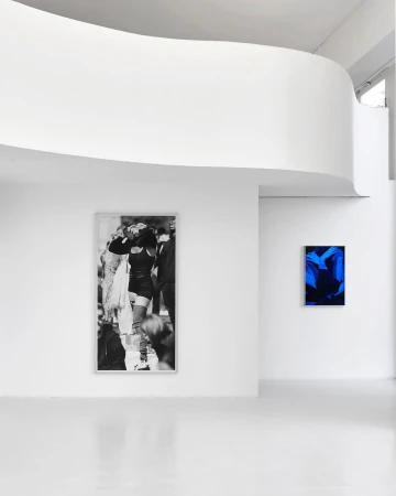 Art gallery interior featuring a black and white fashion photograph and a vibrant blue abstract artwork displayed on white walls.