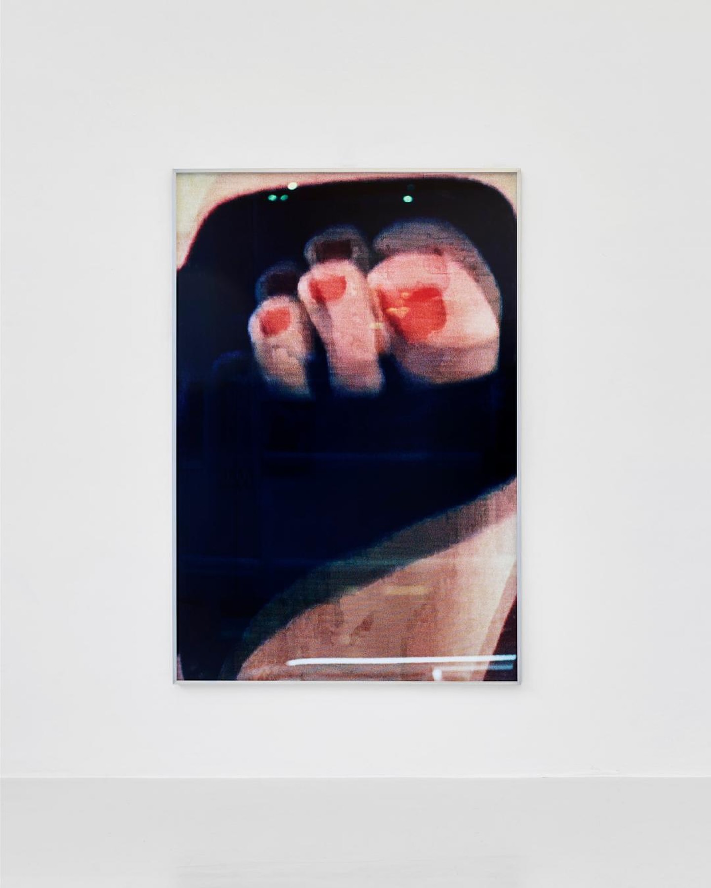 Photograph of framed foot art print on white wall with gray floor in an art gallery. The artwork has red painted toenails.