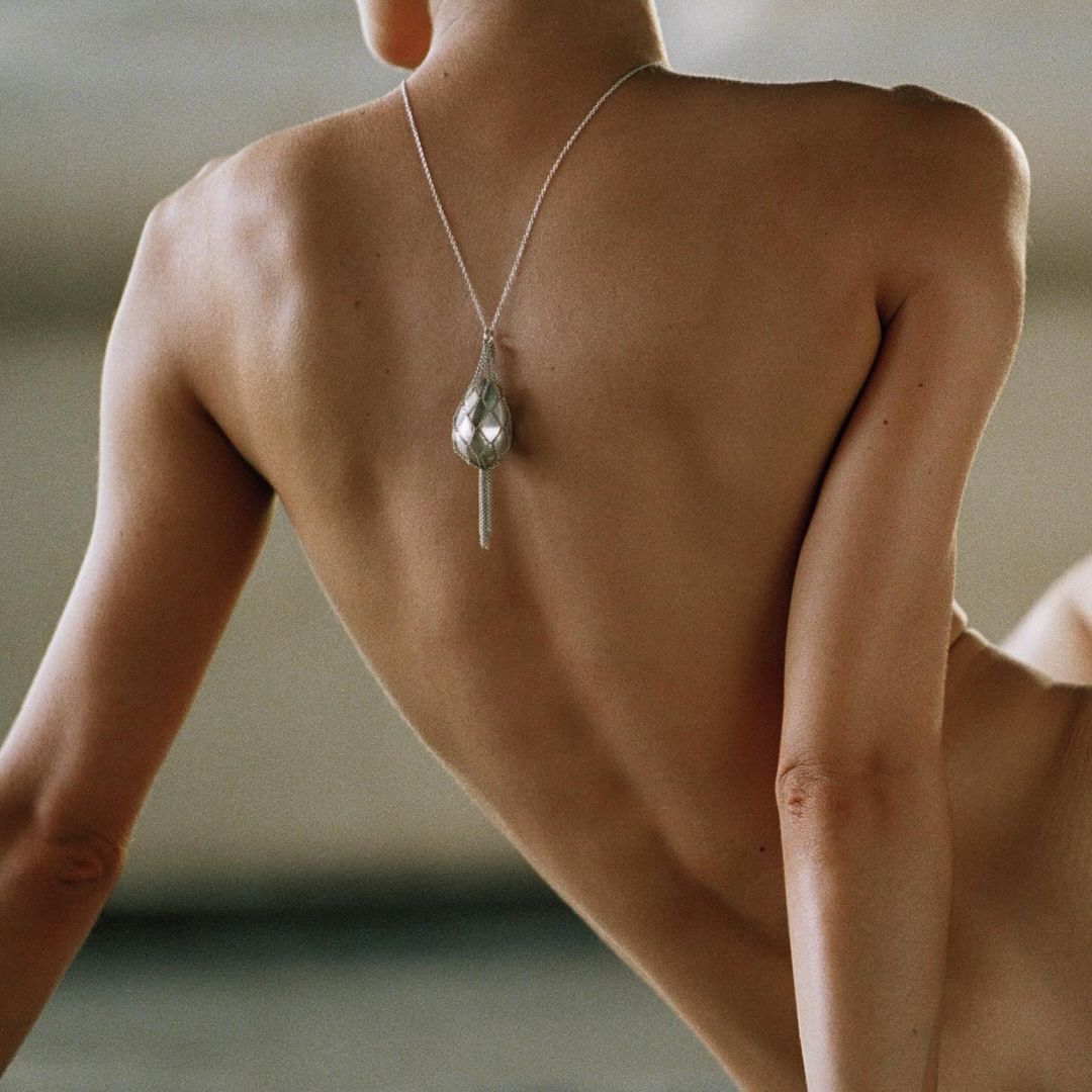 Back view of an adult female wearing a silver pendant necklace in a minimalist fashion or beauty shot, emphasizing jewelry and skin.