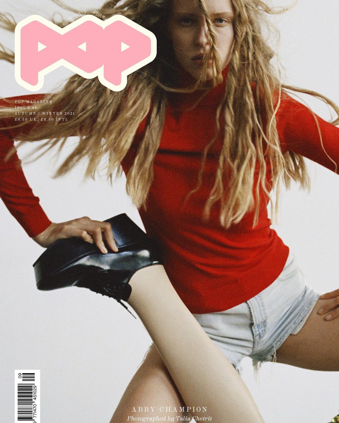 Magazine cover featuring a model with blonde dreadlocks wearing a red shirt and denim shorts, highlighted by a black platform shoe.