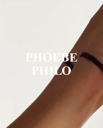 Closeup of fair skin forearm and hand against a white background, with a thin black choker bracelet on the wrist, and brand text overlay.