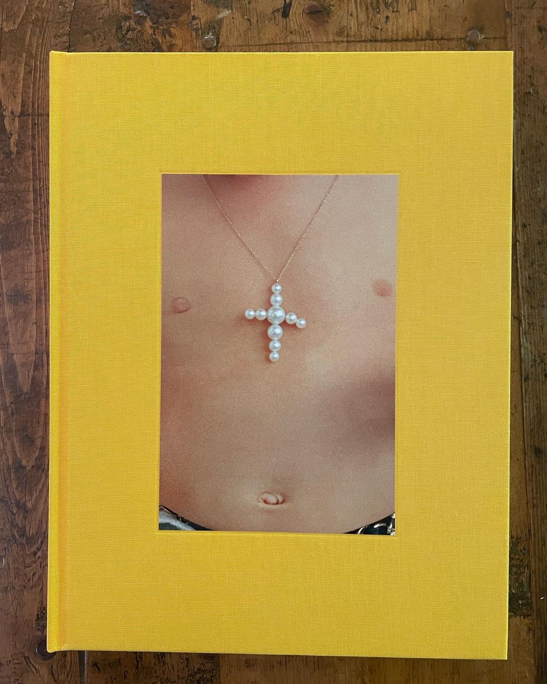 Close up of book cover featuring a person's torso with a pearl cross necklace, set against a bright yellow textured background.