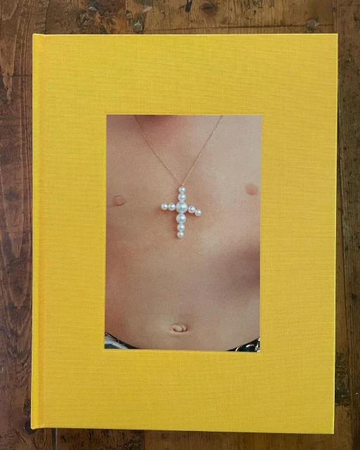Close up of book cover featuring a person's torso with a pearl cross necklace, set against a bright yellow textured background.