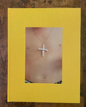 Close up of book cover featuring a person's torso with a pearl cross necklace, set against a bright yellow textured background.