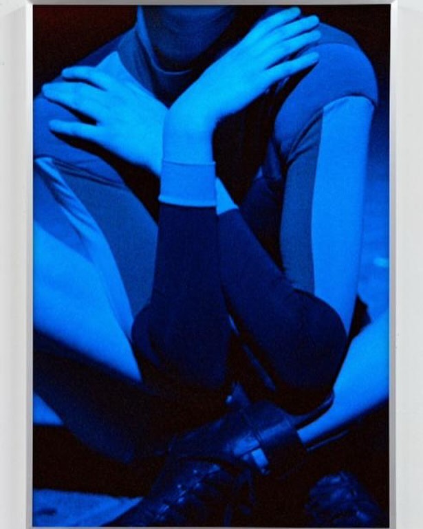 Person in blue outfit posing with arms crossed and high heels in an indoor setting with cool blue lighting, creating a stylish portrait.