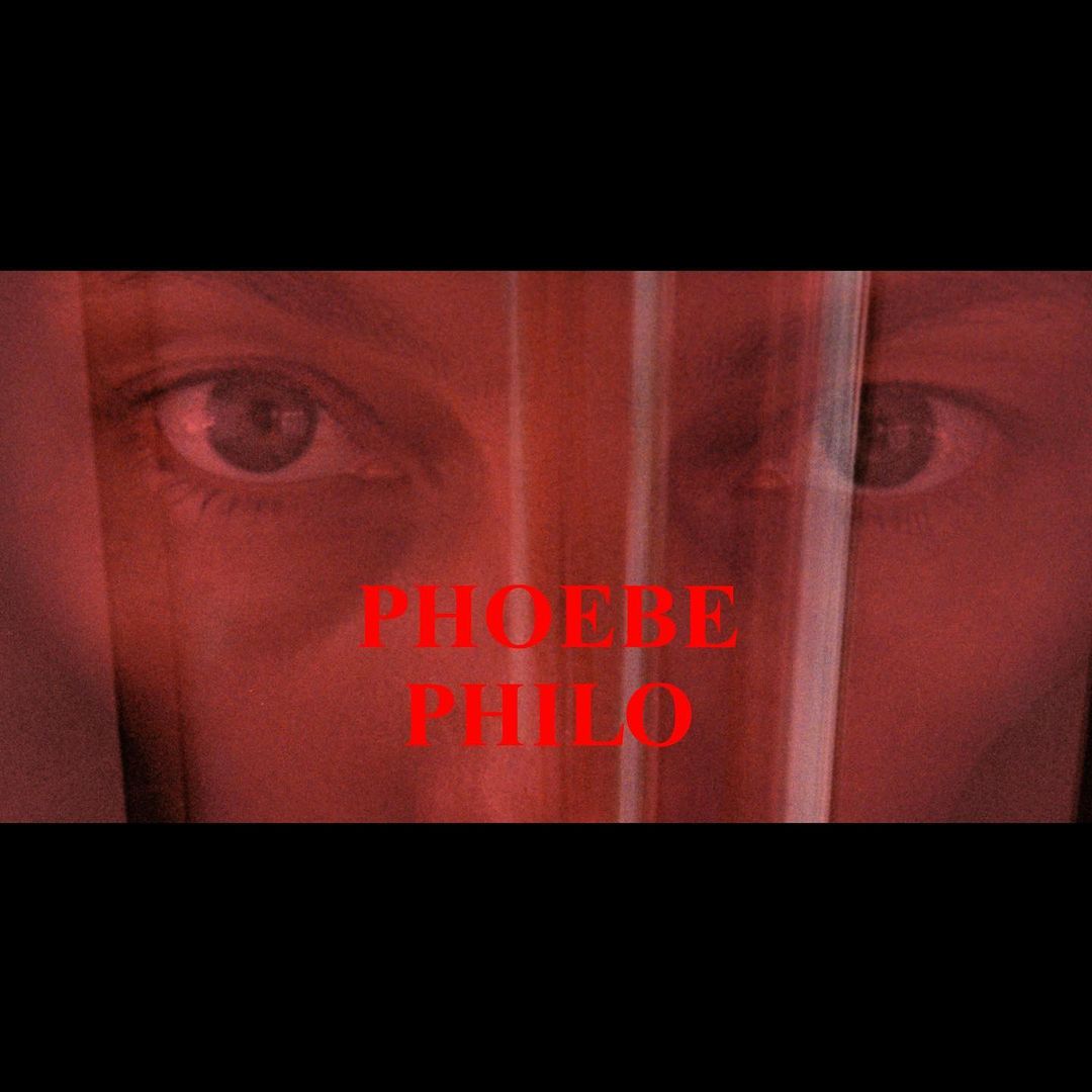Close-up of a person's face partially obscured by a sheer material, with the text 'PHOEBE PHILO' overlaid in red.