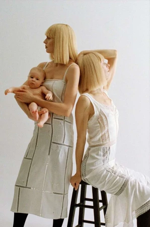 Two adult women with matching blonde bob haircuts and a baby in a studio setting, wearing slip dresses against a white backdrop.