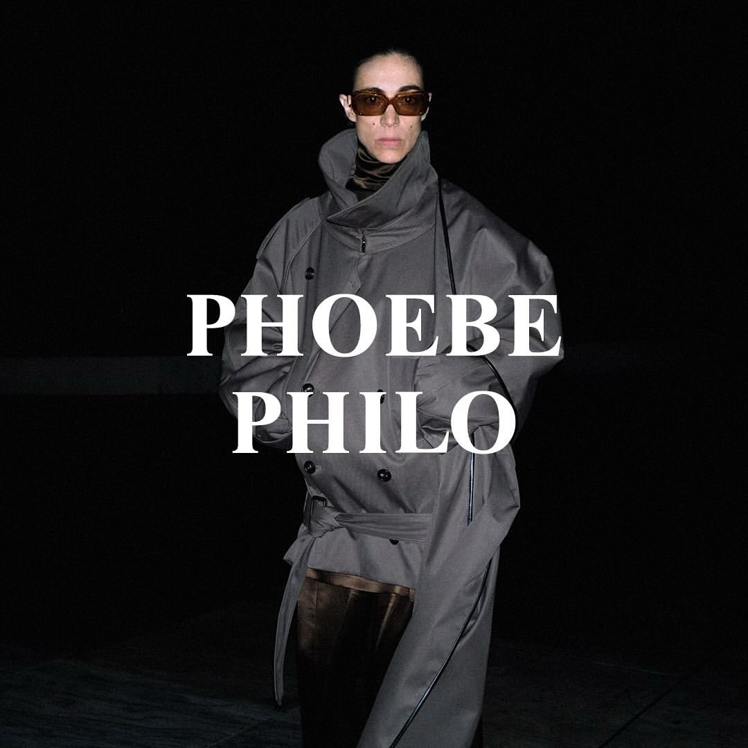 Fashion portrait of an adult female wearing a gray trench coat and brown sunglasses against a dark background with white text overlay.