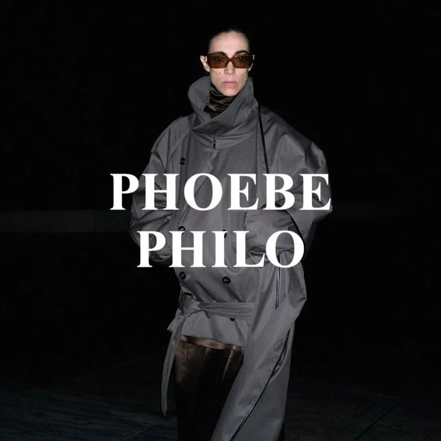 Fashion portrait of an adult female wearing a gray trench coat and brown sunglasses against a dark background with white text overlay.