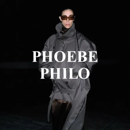 Fashion portrait of an adult female wearing a gray trench coat and brown sunglasses against a dark background with white text overlay.