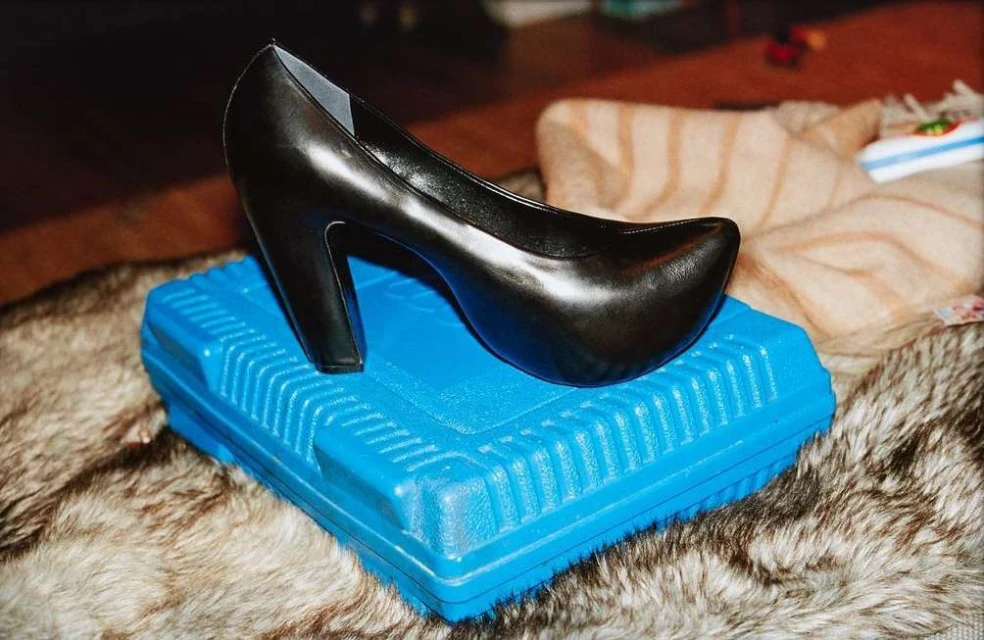 Elegant black high-heeled pump sitting on a bright blue rectangular plastic box, placed on a faux fur surface.