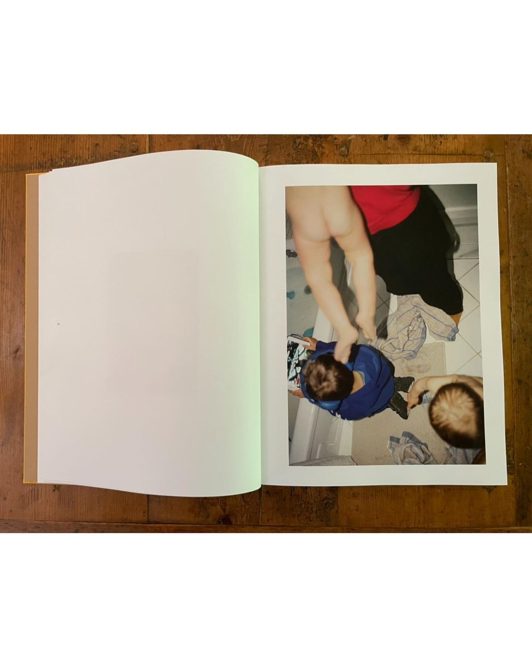 Child standing on another child's back indoors, in photo book, family photo album on wooden table. Top down perspective, daytime.