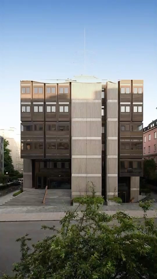 Exterior facade of a modern brutalist concrete building with large grid windows and steps leading to the entrance.