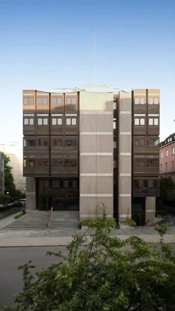 Exterior facade of a modern brutalist concrete building with large grid windows and steps leading to the entrance.