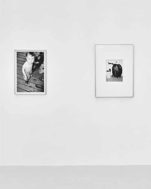 Black and white photography of framed pictures hanging on a wall, one depicting a child, the other an industrial object.