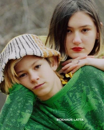 Two young models posing closely together, one wearing a green sweater and bucket hat, photographed by Talia Chetrit