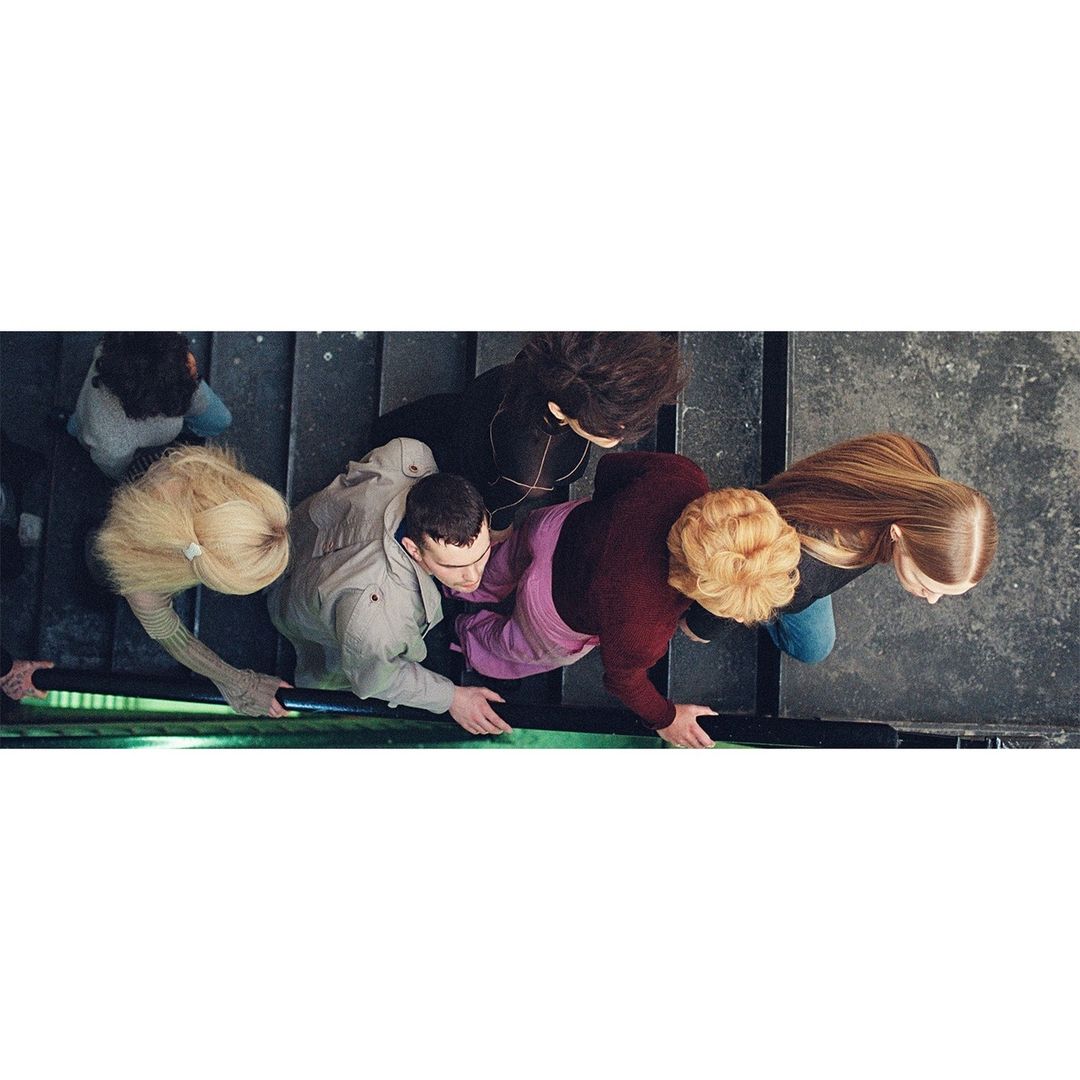 High-angle view of a group of five people, including adult women and a man, standing on a staircase with concrete and a metal rail.