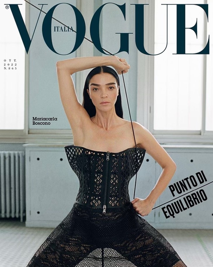 Vogue Italia cover featuring Mariacarla Boscono in a black mesh corset and pants, striking a pose in a minimalist indoor setting.