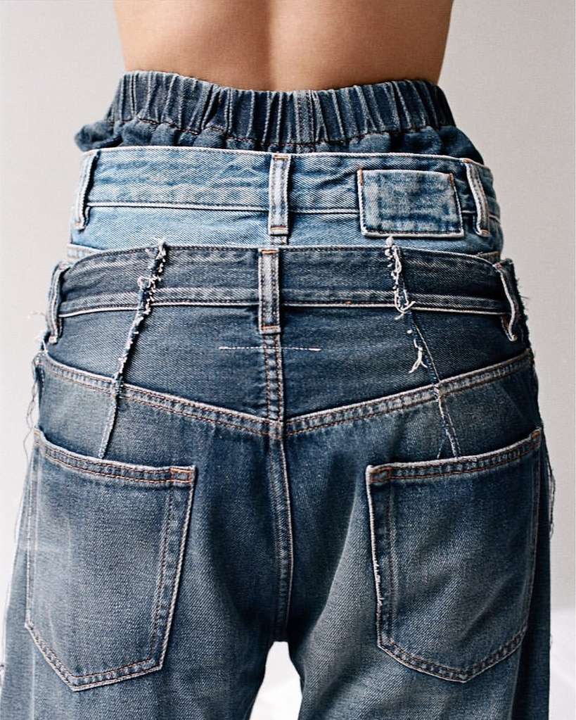 Rear view of a person wearing layered blue denim jeans, showcasing innovative and stylish fashion design against a plain background.