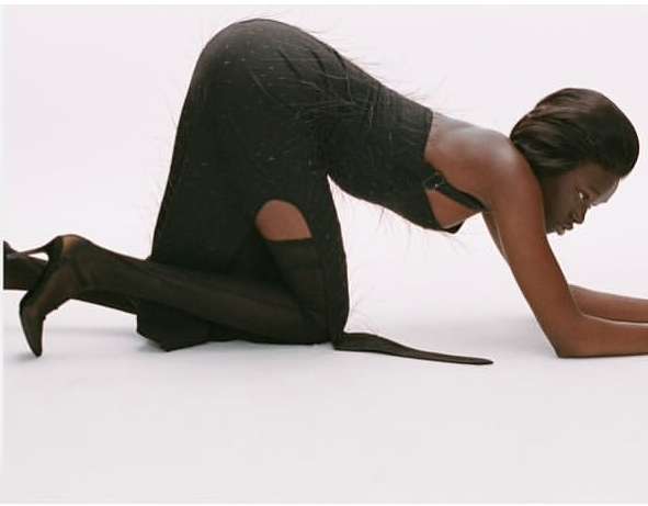 Woman in a long, black dress poses on all fours in a studio. She is kneeling with arms straight and head down against a white background.