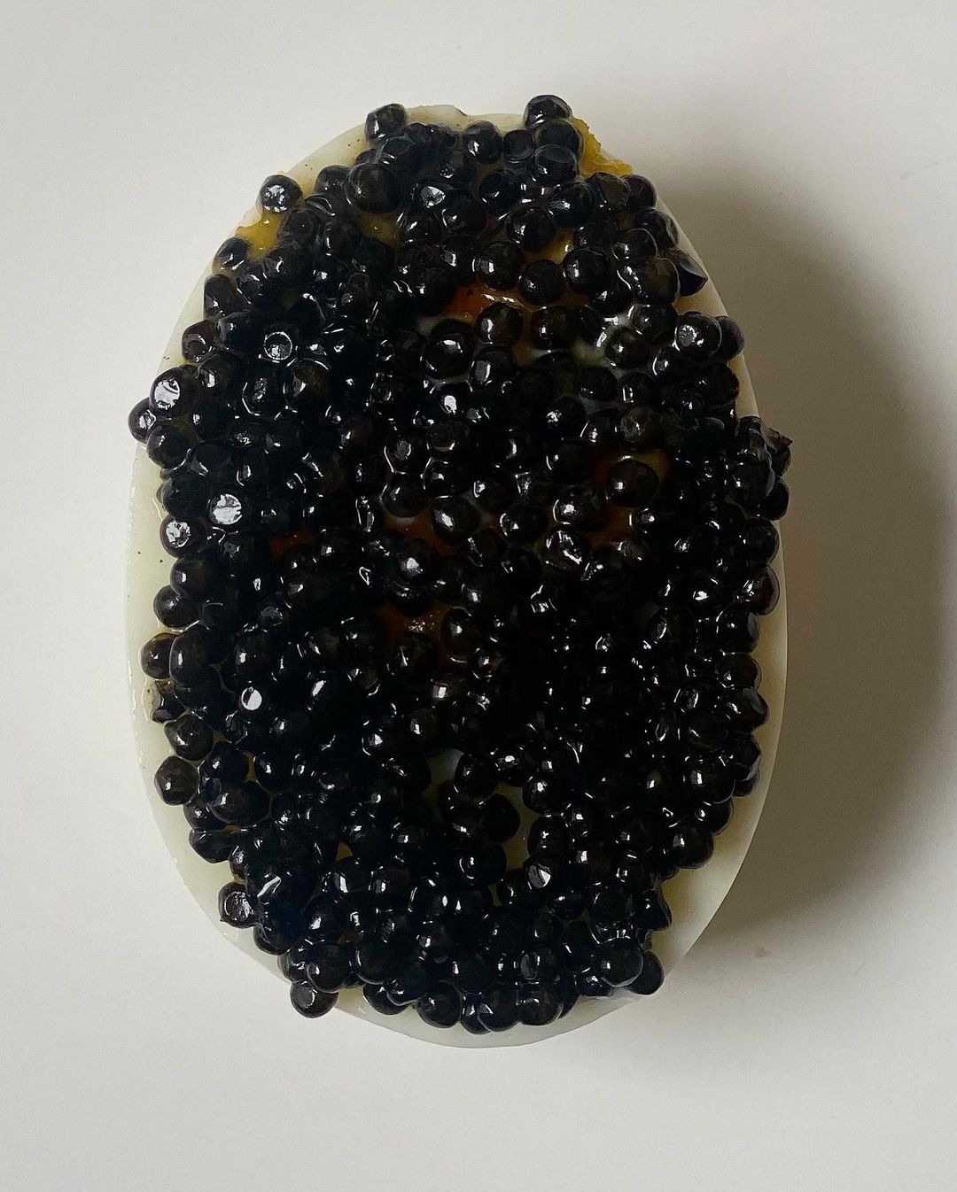 Caviar tops a halved boiled egg, creating a striking contrast between the white egg and the shiny black pearls.