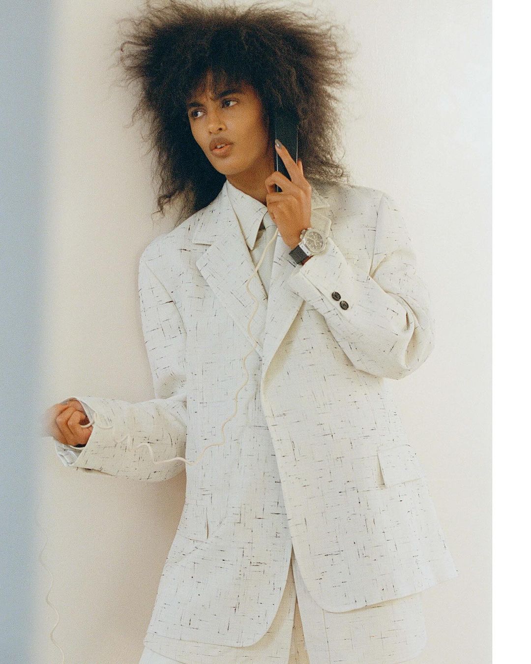 Model with voluminous dark hair wearing a white patterned blazer on phone, photographed by Tanya and Zhenya Posternak