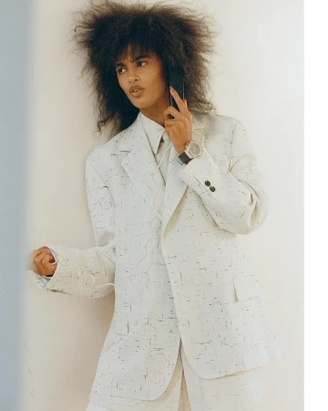 Model with voluminous dark hair wearing a white patterned blazer on phone, photographed by Tanya and Zhenya Posternak
