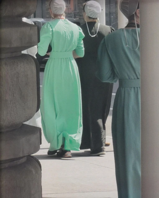 Three women in traditional dresses and head coverings stand on a sidewalk near a carved stone pillar, capturing a blend of fashion and culture.