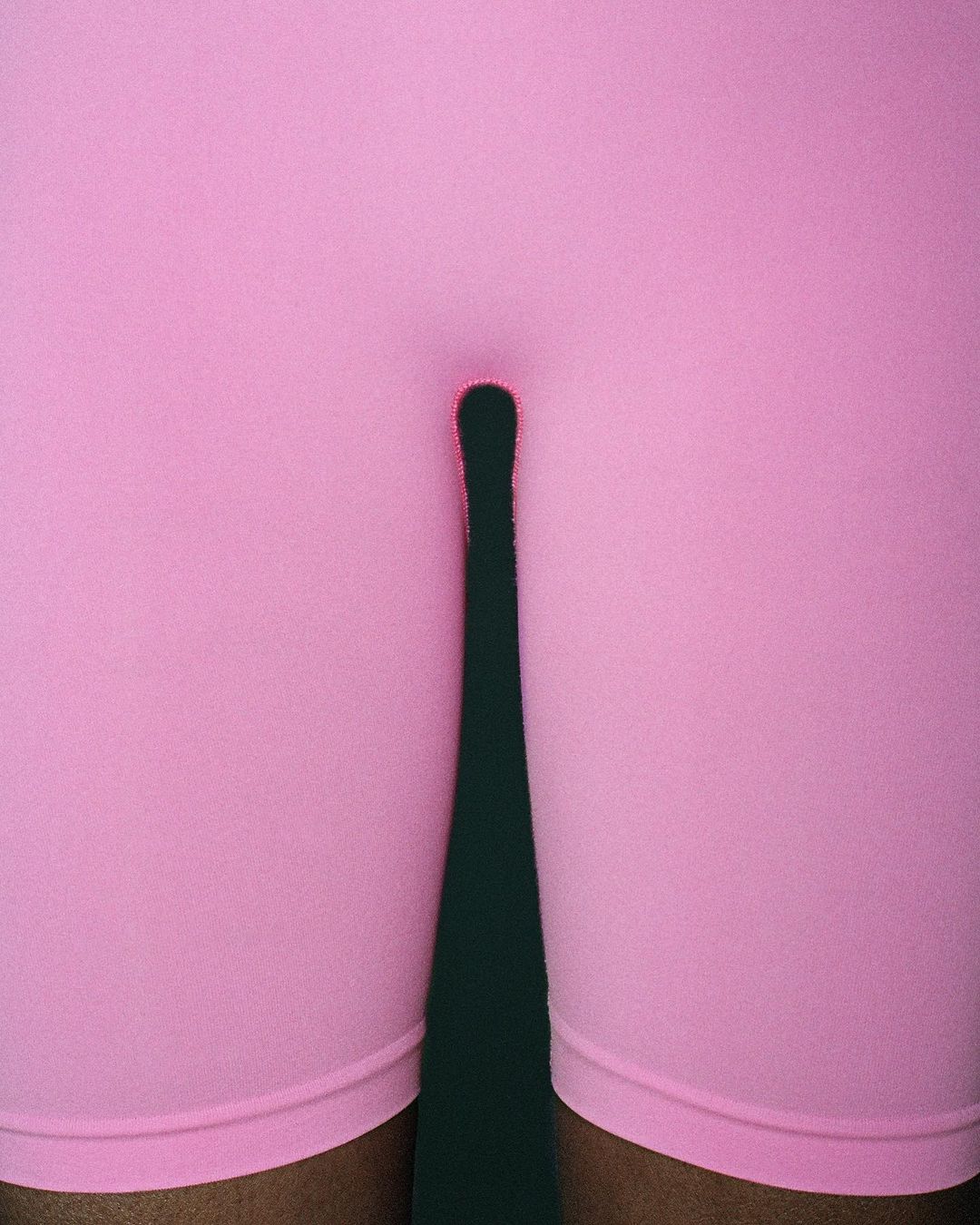 Close-up of person in pink shorts with shadow on dark green background, fashion, athletic wear, fitness apparel, legs.