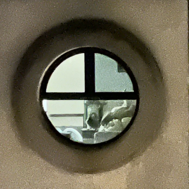 Close-up of an indoor window in a wall, providing a view of interior space with furniture and objects.