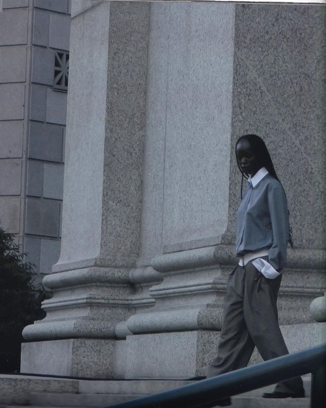 An African-American woman walks down gray stone stairs in an urban setting wearing a blue button-down shirt and gray slacks.