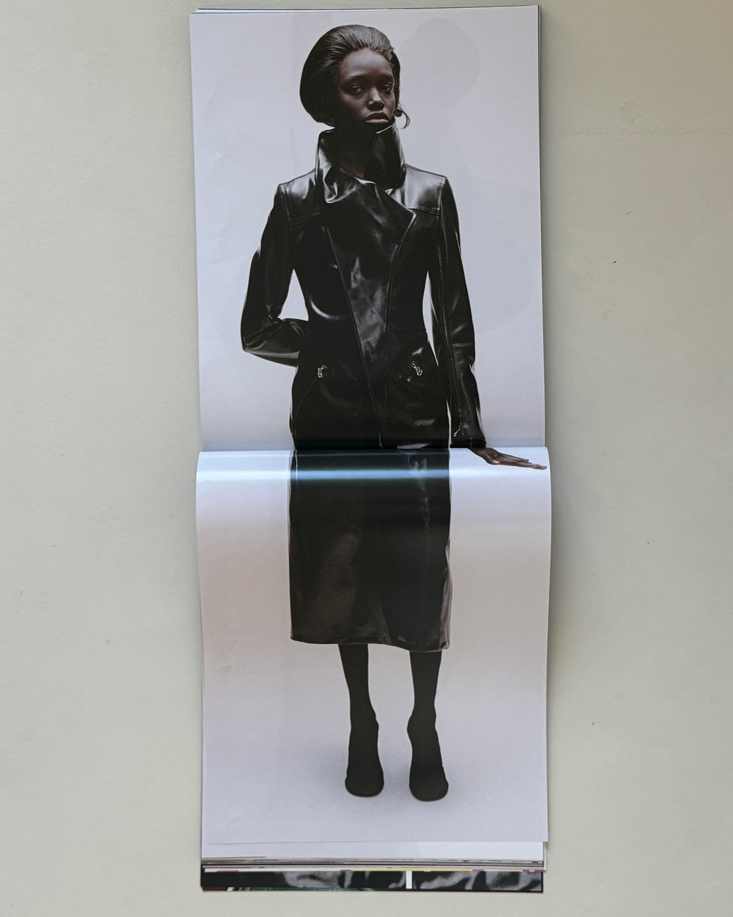 A print photograph shows a dark-skinned woman wearing a black leather jacket and skirt against a grey backdrop in a studio setting.