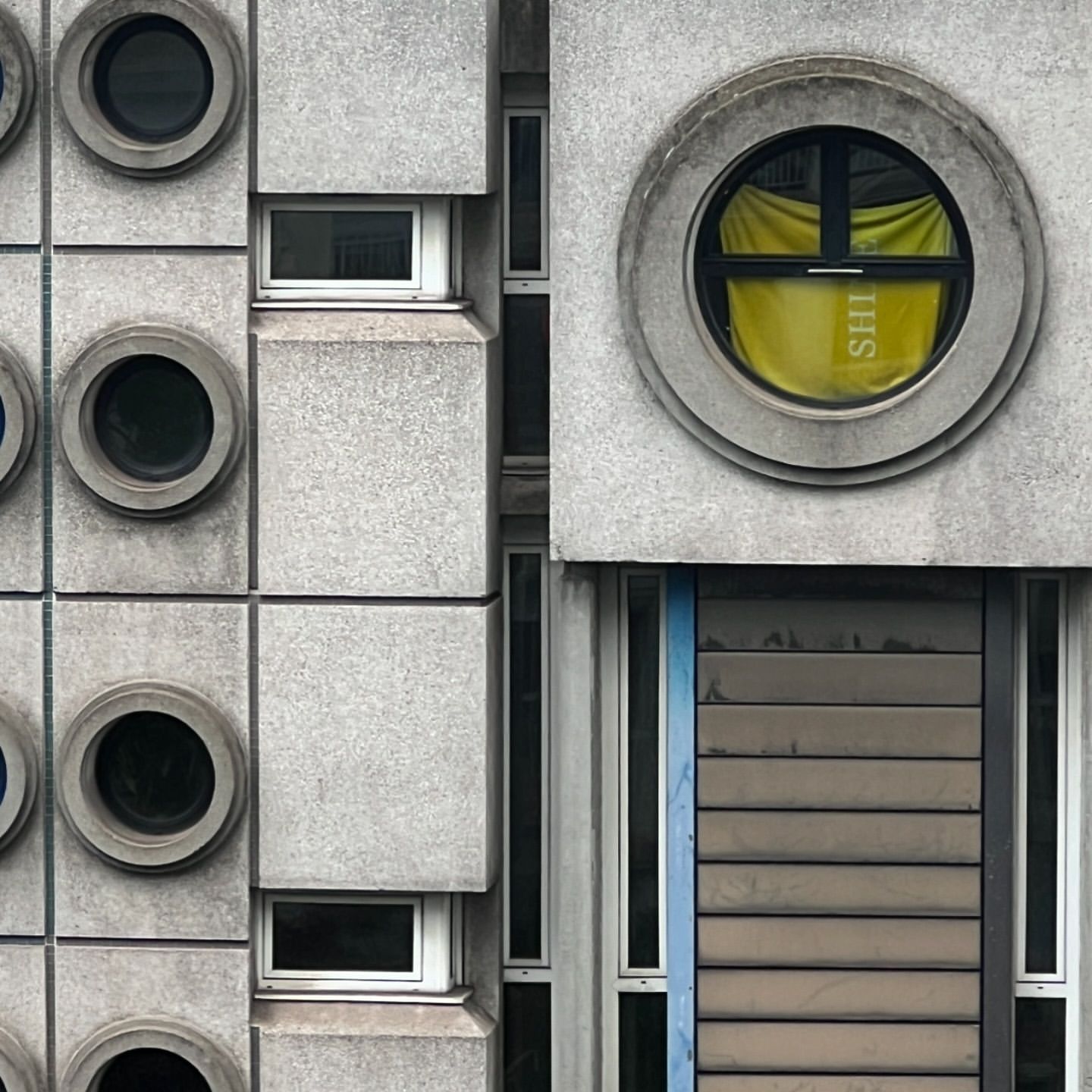 Architectural photo of a concrete building facade with round and rectangular windows, showcasing minimalist design and geometric shapes.