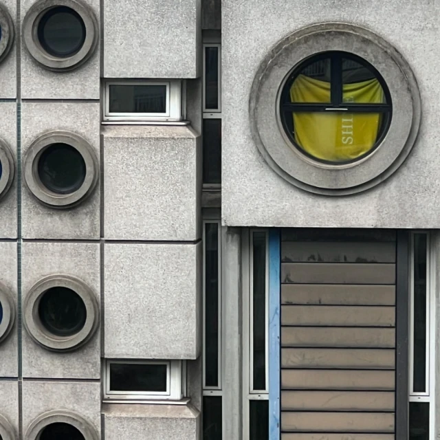 Architectural photo of a concrete building facade with round and rectangular windows, showcasing minimalist design and geometric shapes.