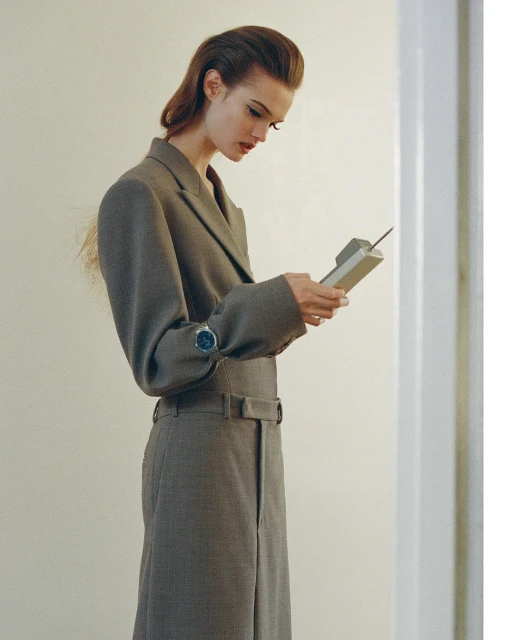 Elegant woman in a grey suit holds a vintage brick cell phone in an indoor setting, showcasing fashion and technology elements.